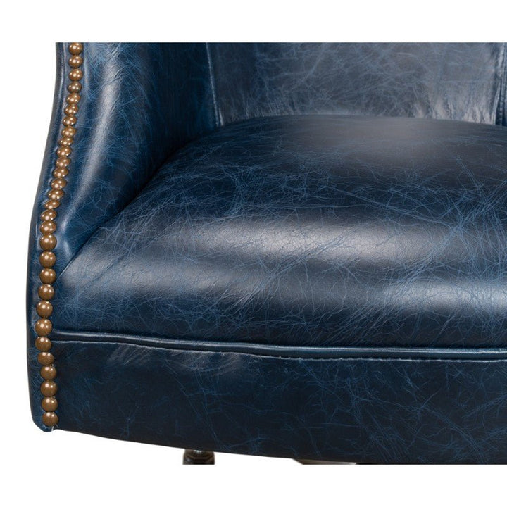 Close-up of the Sarreid Andrew Jackson Desk Chair in Chateau Blue, highlighting its textured pure aniline top-grade cowhide leather surface. The chair features brass nailhead trim along the side, adding a decorative touch.