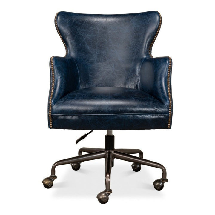 The Andrew Jackson Desk Chair, Chateau Blue by Sarreid is a dark blue leather office chair equipped with a high backrest and winged armrests. It features nailhead trim along the edges and is mounted on a metal swivel base with five caster wheels for easy mobility. This chair also includes an adjustable height lever.