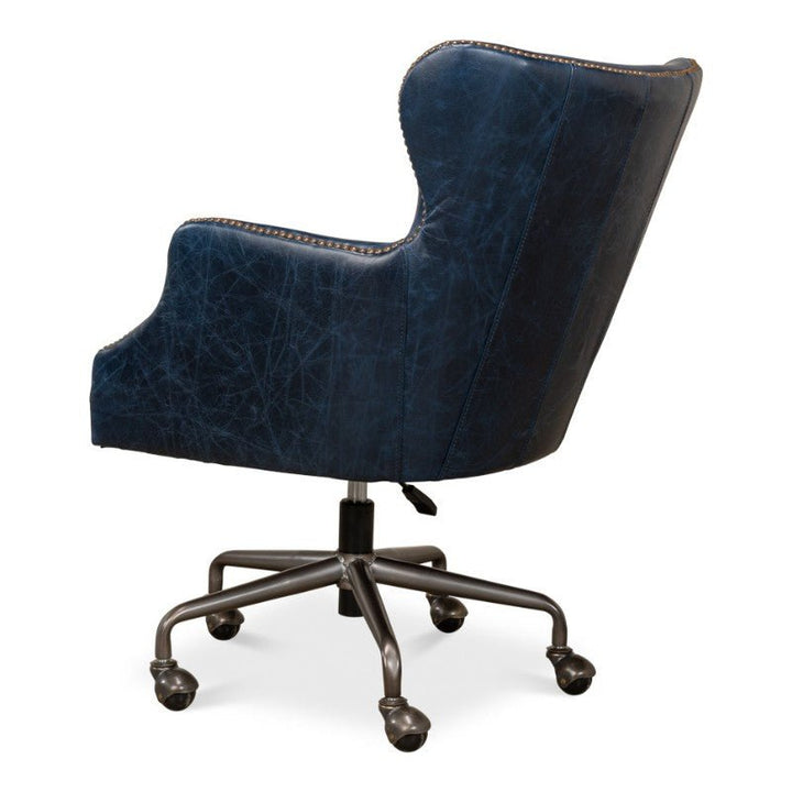 The Andrew Jackson Desk Chair, Chateau Blue by Sarreid boasts a high back and winged sides adorned with nailhead trim. Crafted from pure aniline top-grade cowhide leather in a striking navy blue, this elegant chair is set on a five-pointed metal base equipped with caster wheels and features a height-adjustable lever.