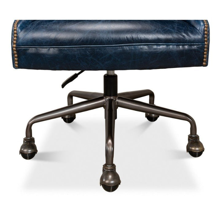 Close-up of the lower part of the Sarreid Andrew Jackson Desk Chair in Chateau Blue, showcasing its metal base with five caster wheels and an adjustable lever. The seat is upholstered with pure aniline top-grade cowhide leather, accented by brass nailhead trim along the edge for added detail.