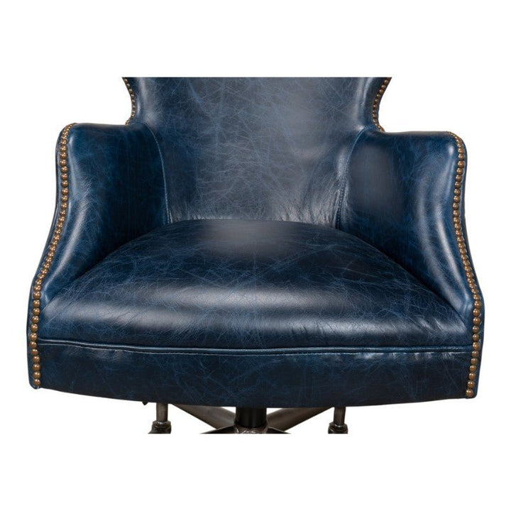 A close-up view of the Sarreid Andrew Jackson Desk Chair in Chateau Blue, crafted from pure aniline top-grade cowhide leather and featuring brass stud detailing along the edges of the armrests and backrest. The chair boasts a padded seat and is showcased against a plain white background.