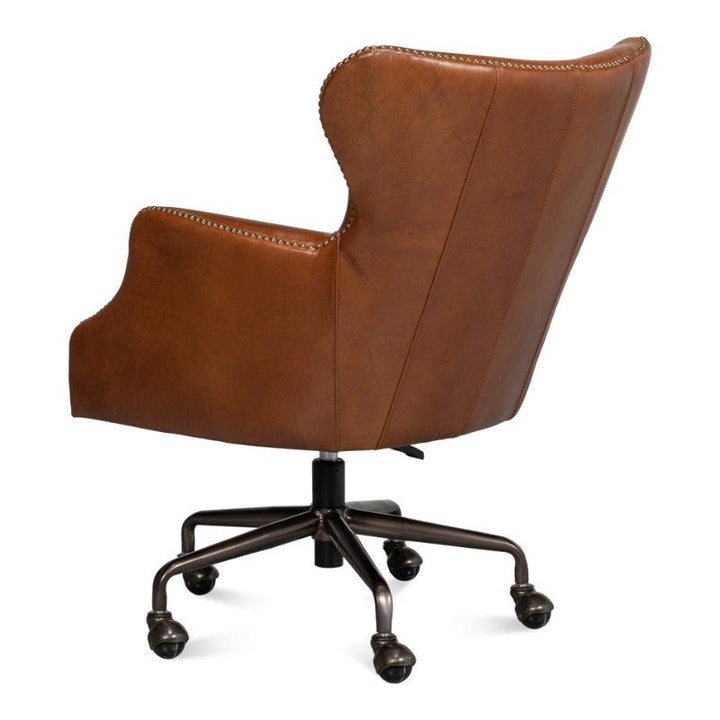 A brown Andrew Jackson Desk Chair in Havana Leather by Sarreid, featuring padded armrests and a curved backrest, viewed from behind. The chair showcases nailhead trim along the edges and is supported by a metal base with five caster wheels.