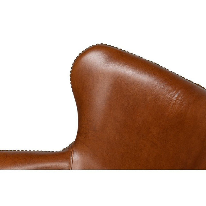 Close-up view of the Andrew Jackson Desk Chair in Havana Leather by Sarreid, showcasing a smooth, curved design. The stitching detail is visible along the edge, emphasizing the chair's craftsmanship and transitional design.