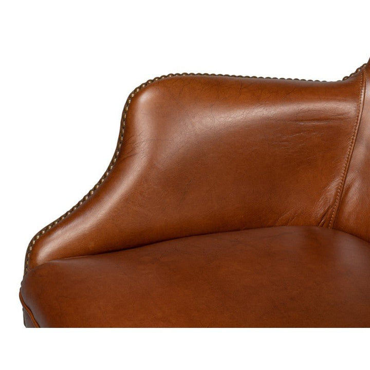 Close-up of a Sarreid Andrew Jackson Desk Chair in Havana leather, highlighting its smooth, curved armrest adorned with visible seams and decorative nailhead trim. The slightly distressed, vintage appearance of the leather complements the plain white background.