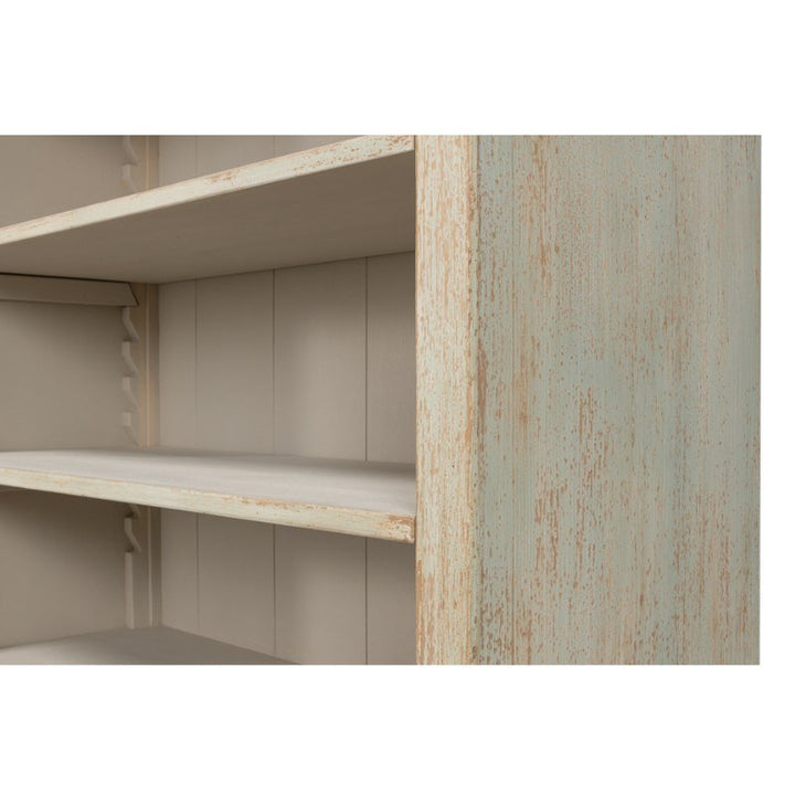 Close-up of the Angelique Bookcase by Sarreid, featuring a multi-tiered wooden design crafted from reclaimed pine with a light beige and distressed mint green paint finish. This bookshelf offers adjustable shelves, embodies a rustic, weathered appearance, and exudes coastal charm.