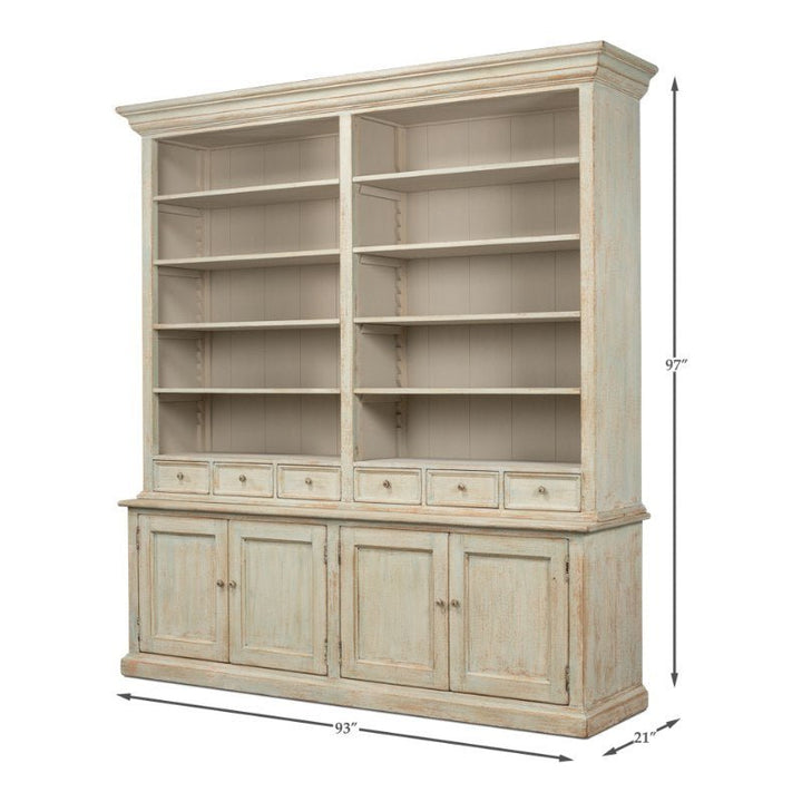 The Angelique Bookcase by Sarreid is a spacious wooden bookshelf with a distressed finish and Coastal charm. It features six upper shelves divided into two sections, four small central drawers, and four lower cabinet doors. Crafted from reclaimed pine with an Antique Blue Wash, this bookcase measures 93 inches wide, 21 inches deep, and 97 inches high.