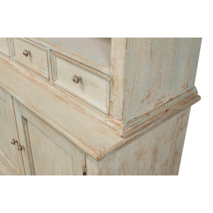 A close-up of the Angelique Bookcase by Sarreid, featuring a weathered, antique-style design with a distressed light blue finish. The reclaimed pine wood showcases a rustic, vintage look. The lower section with double doors and upper drawers adorned with metal knobs add coastal charm to space.