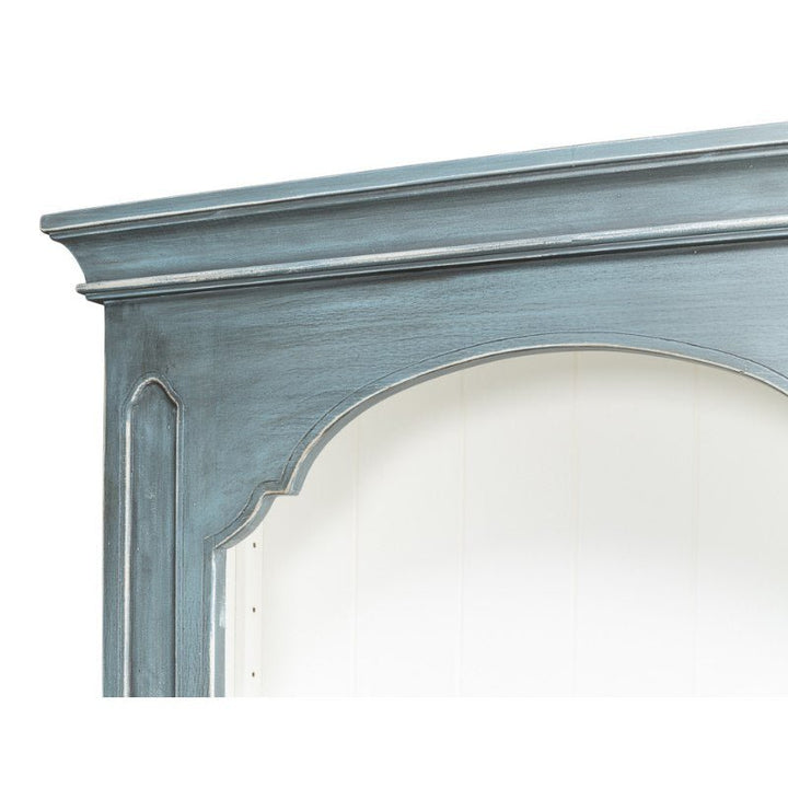 Close-up of the top section of the Banner Bungalow Bookcase by Sarreid, painted in distressed turquoise with a white interior. The bookcase features a decorative, curved arch design and recessed panel detailing at the corners, reminiscent of rustic Russian pine craftsmanship.