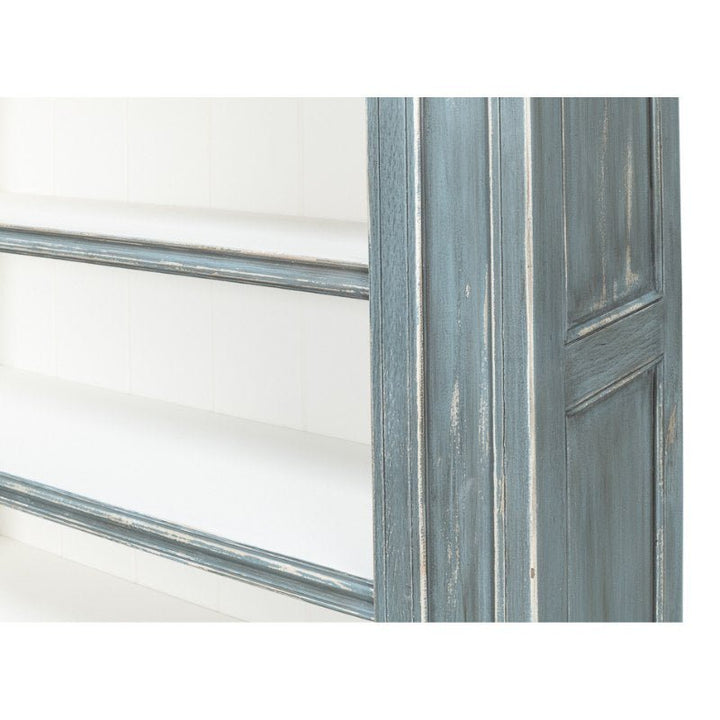 A close-up shot of the Sarreid Banner Bungalow Bookcase showcases its distressed blue finish and white interior shelves, exuding a rustic and vintage charm. Crafted from Russian pine, the image highlights the bookcase's texture and paint in exquisite detail.