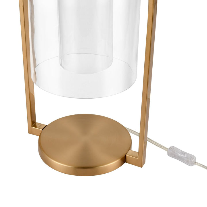 Introducing the Elk Home Bell Jar 28'' High 1-Light Desk Lamp, boasting a modern farmhouse aesthetic. It features a bell jar-style cylindrical glass shade elegantly supported by a sleek frame and base finished in aged brass. The design includes a power cord and clear switch at the bottom for convenient access.