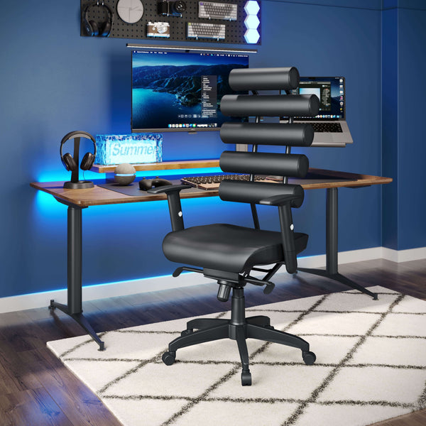 A sleek, modern high back office chair from Zuo, named the Black Office Chair - Unico, with a unique segmented backrest and lumbar support sits on a white and black patterned rug in front of a stylish desk setup. The desk features a dual-monitor setup with ambient blue lighting and various tech accessories against a blue wall background.