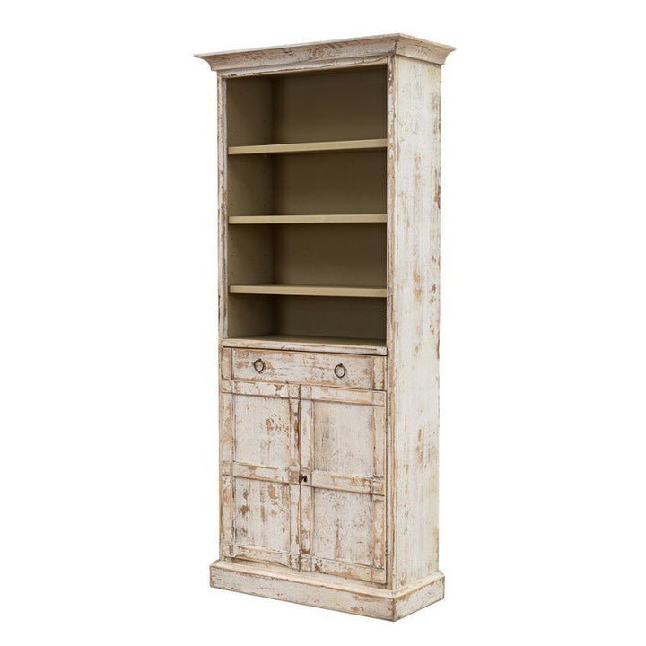 The Bookcase With Doors, Disrupted White by Sarreid is a tall, rustic white bookcase featuring a distressed finish. It offers four open shelves at the top, a middle section with one drawer, and two closed doors at the bottom. This solid pine bookcase boasts a vintage, weathered appearance.