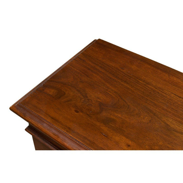 Close-up of the top corner of a polished wooden table. The surface is smooth with visible wood grain patterns, showcasing a rich, warm walnut color. Made from solid walnut, the table's beveled edge presents a classic and refined appearance reminiscent of the Sarreid Carmel-By-The-Sea Bookcase.