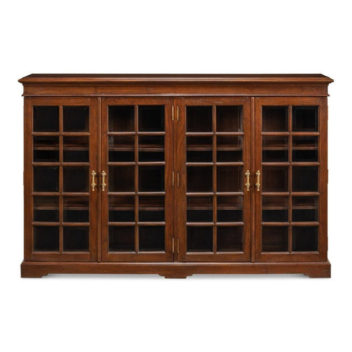 The Sarreid Carmel-By-The-Sea Bookcase is a large, rectangular piece featuring four glass-paneled doors with grid-like wooden frames and antique brass accents. Made of solid walnut, it has a polished dark finish and boasts a classic design. The interior includes multiple shelves that are perfect for storage or display.