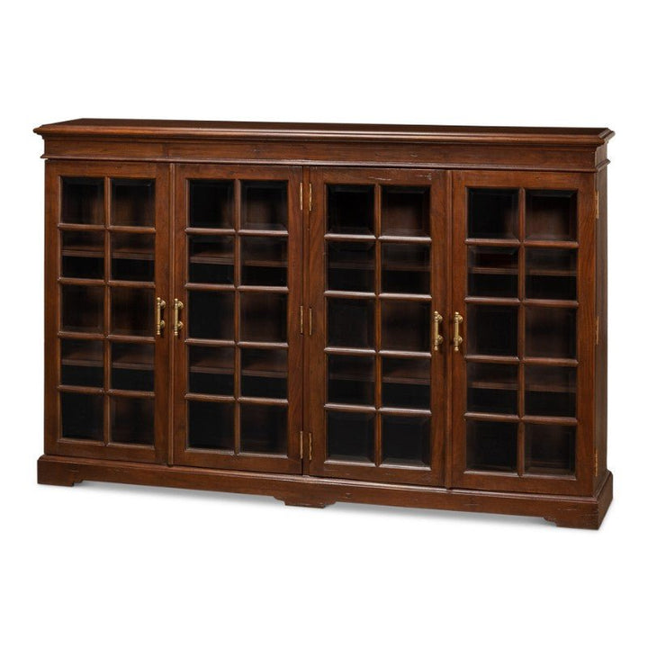 The Carmel-By-The-Sea Bookcase, Walnut by Sarreid is a solid walnut wooden cabinet featuring a dark brown finish and four glass-paneled doors adorned with antique brass accents. The cabinet doors have a grid pattern and include multiple shelves inside, making it perfect for storage or display. This piece reflects a classic, elegant style.