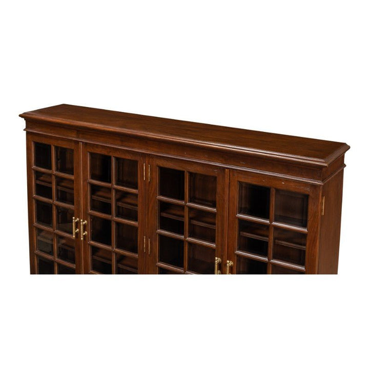 The Carmel-By-The-Sea Bookcase, Walnut by Sarreid features a solid walnut construction with a smooth top surface and three glass-paneled doors. Each door showcases a grid design and antique brass accents, revealing multiple inner shelves. This bookcase exudes a classic and elegant appearance.