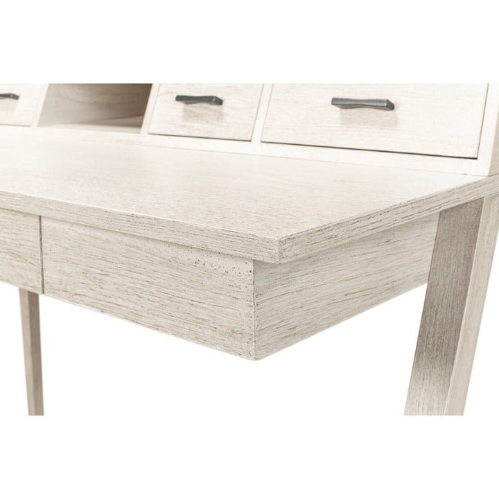 A close-up view of the Covet Desk - Sarreid by Sarreid in an Ivory Bianca finish showcases part of its light-colored wooden tabletop, three drawers with dark handles, and a portion of its slanted legs. The modern desk features a minimalist design with a smooth surface and clean lines, highlighting its practical functionality.