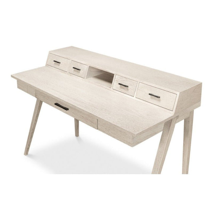 The Covet Desk by Sarreid is a sleek and modern piece with an Ivory Bianca finish. This wooden desk features two tiers: the upper tier includes three small drawers and a center cubbyhole, while the lower tier offers a large drawer. Standing on four tapered legs, this desk combines practical functionality with stylish design, making it perfect for any workspace.