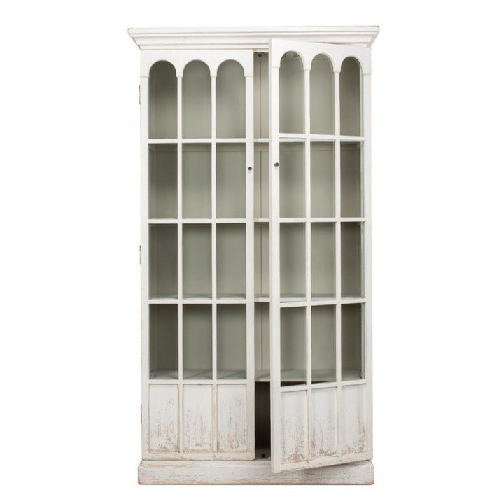 The Edgar Allan Glass Bookcase by Sarreid is a white, vintage wood cabinet with two glass-paned doors slightly ajar, revealing empty interior shelves. The bookcase features an arched design on the top section of the doors and a slightly distressed whitewash finish, adding to its rustic charm reminiscent of traditional design.