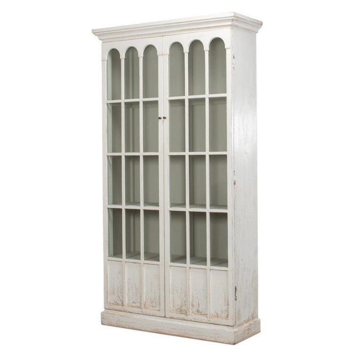 The Edgar Allan Glass Bookcase by Sarreid is a tall, white, reclaimed pine bookcase featuring two glass-paneled doors with an arched design at the top of each door. This cabinet showcases a slightly distressed, whitewash finish, imparting a rustic, vintage look. It stands on a broad base and includes multiple interior shelves for traditional design elegance.