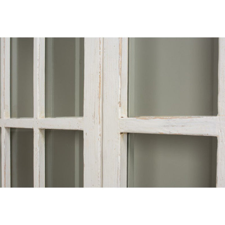 An up-close view of the Edgar Allan Glass Bookcase by Sarreid, featuring a vintage, whitewashed wooden structure with multiple glass panes. The slightly distressed paint finish imparts a rustic charm to the bookcase. The blurred background behind the glass emphasizes its traditional design details.