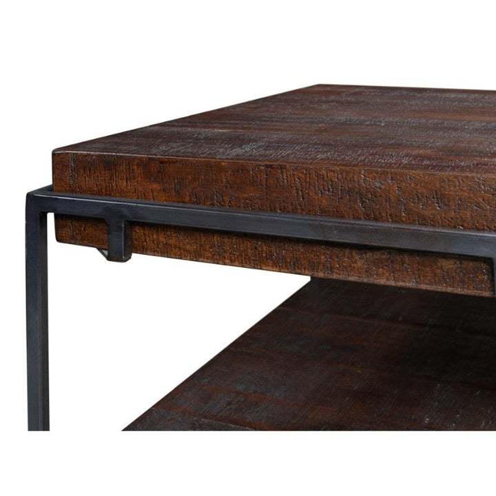 Close-up image of the Ernest Desk by Sarreid, featuring a dark mango wood square top. The desk boasts a textured surface and is supported by a minimalist black iron frame. This industrial piece has a rectangular profile and includes a convenient shelf beneath the tabletop, ideal for any home office setup.