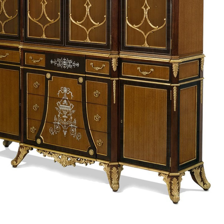 The Eucalyptus and Gold Gilt Breakfront Bookcase by Aston Court boasts exquisite gold gilt detailing and dark accents. This piece features decorative carvings, intricate inlays on the cabinet doors, and gold-accented legs. Multiple doors and drawers are visible, with an elegant urn design on the central drawer panel.