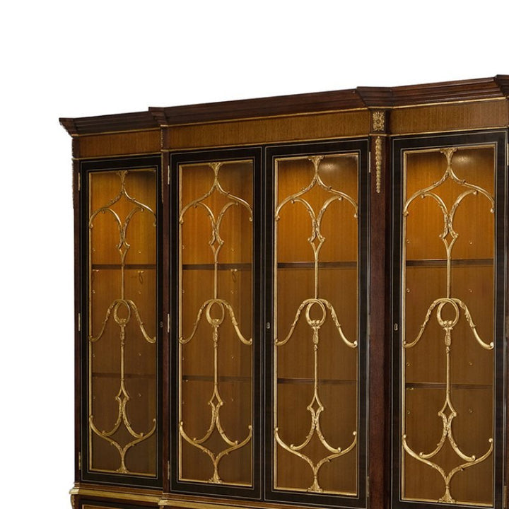 This eucalyptus and gold gilt breakfront bookcase from Aston Court features four glass-paneled doors adorned with intricate gold gilt detailing. The interior includes wooden shelves, highlighting elegant, classic craftsmanship with rich eucalyptus wood tones. The top of the bookcase has a slightly protruding cornice, enhancing its timeless appeal.