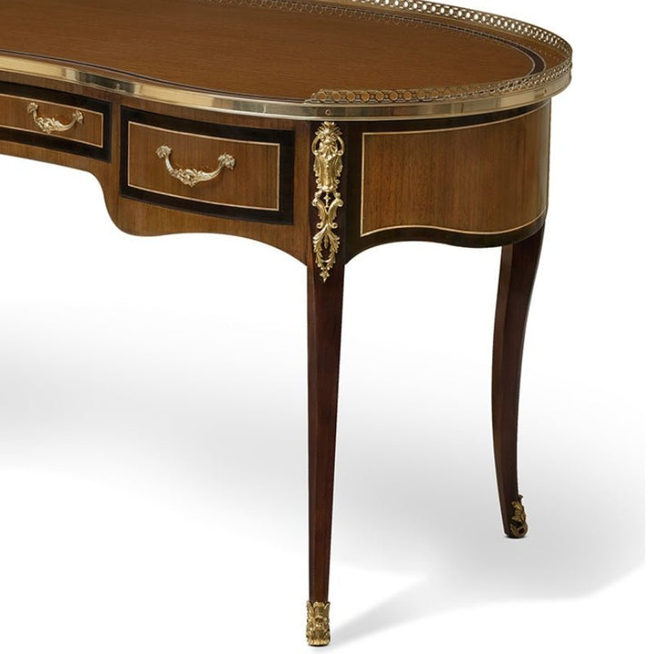 Introducing the Eucalyptus Lady's Kidney Writing Desk from Aston Court, a sophisticated piece featuring two drawers adorned with ornate brass handles and intricate brass detailing on the corners and legs. This exquisite desk boasts a dark wood finish and a luxurious eucalyptus wood surface, accentuated by a brass gallery elegantly lining the edge of the top surface.