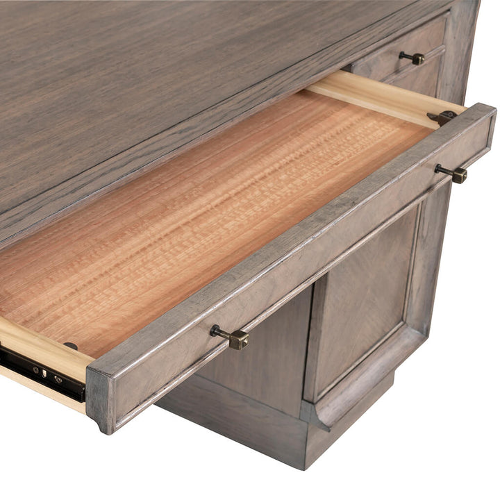 A close-up of a partially open drawer in the Expedition Pedestal Desk 60" by Fairfield Chair. The drawer features a light wood interior and a darker grayish exterior with a weathered finish, evoking an Art Deco design. Metal hardware adorns the front, facilitating easy opening.