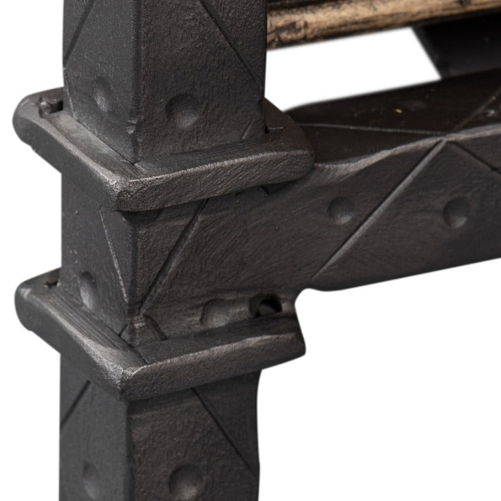 Close-up image of the Game Of Thornes Desk by Sarreid, highlighting a black metal corner bracket with a textured surface and geometric pattern, affixed to reclaimed old wood beams. The rectangular bracket features triangular embossed designs with visible bolts, while the wood showcases a natural, unfinished texture.