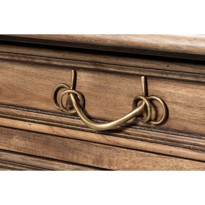 Here's a close-up of the Game Of Thornes Desk by Sarreid, showcasing a rustic wooden drawer adorned with a vintage brass handle. The elegantly curved handle features ornate loops on either side, affixed to the front of the drawer with small brackets. Crafted from reclaimed old wood, the distinctive grain and texture enhance its antique appearance and unique design.