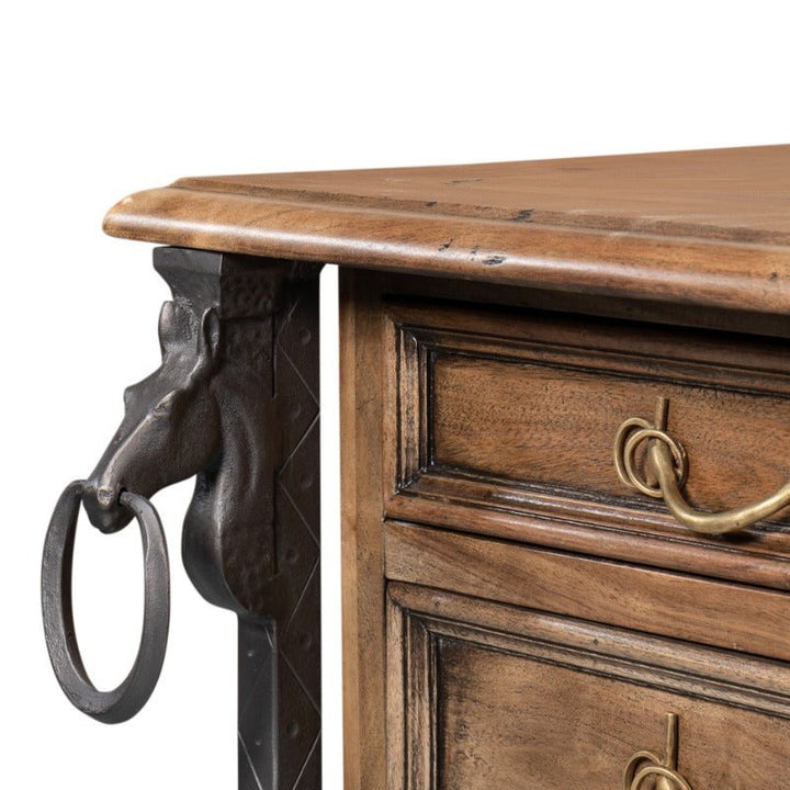 The Game Of Thornes Desk by Sarreid showcases intricate woodwork crafted from reclaimed old wood. It features two visible drawers with brass handles, and the side is embellished with a rustic, black metal horse head complete with a ring hanging from its mouth, contributing to its unique design.