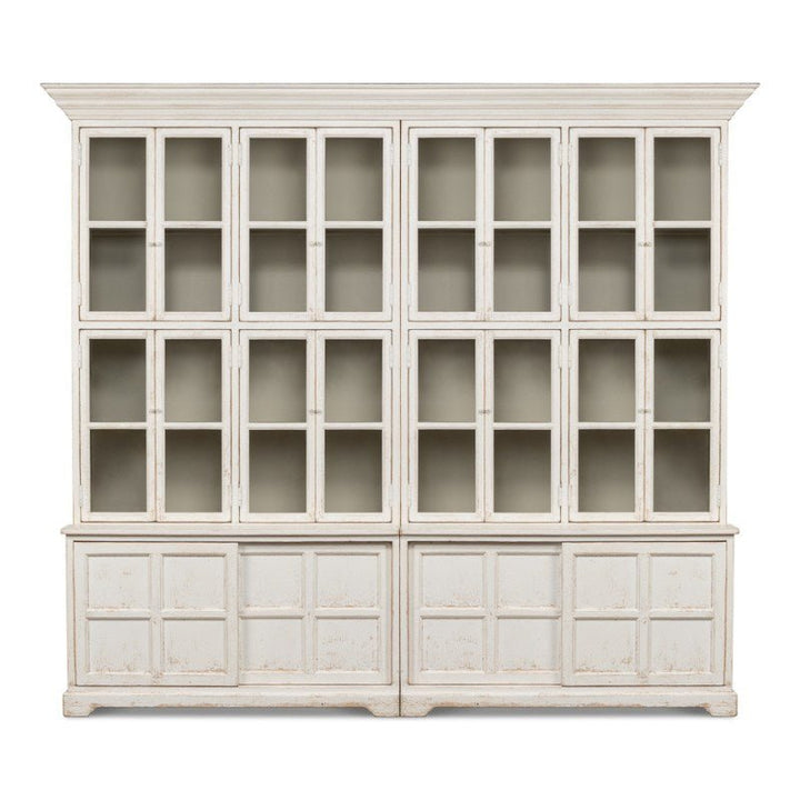 Introducing the Glass Front Bookcase - Sarreid by Sarreid: a large, vintage-style wooden cabinet from our farmhouse collection. It features a distressed white finish with three rows of glass-paneled doors on the upper portion, ideal for displaying cherished items. The lower portion includes solid doors with panel detailing, providing ample storage space.