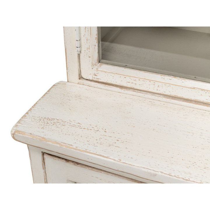 Close-up of the distressed white corner of the Glass Front Bookcase - Sarreid from Sarreid. This bookcase features a glass-fronted section and a weathered paint finish. The surface and edges showcase natural wood textures and aged details, giving it a rustic farmhouse appearance.