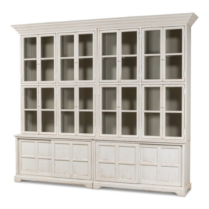 Introducing the Sarreid Glass Front Bookcase, a standout piece from our farmhouse collection. This large, white wooden cabinet boasts a distressed finish that exudes classic rustic charm. The unit features two tiers: the upper section is adorned with twelve glass-paneled doors, perfect for displaying your items, while the lower section includes six solid wood doors for additional storage. Designed to provide ample storage space, this bookcase combines functionality with timeless style.