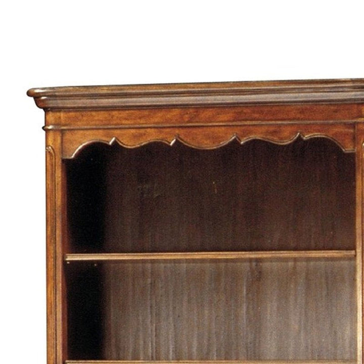 A close-up of the Aston Court Hand Planed Distressed Bookcase showcases its classic style with an intricately carved, ornamental top edge. This dark brown wooden bookcase, featuring one visible shelf and a hand-planed finish, exudes rustic charm.