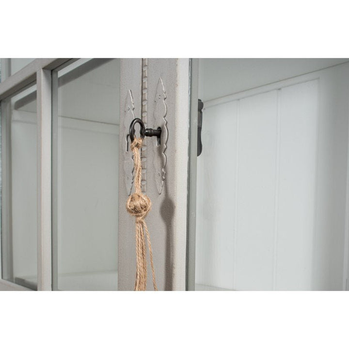 Close-up of the Sarreid Harper Glass Front Bookcase door, featuring a decorative metal latch and rope handle. The intricately detailed latch stands out, complementing the wood construction with its painted finish. This elegant design offers ample storage while the blurred background emphasizes the door's ornate features.