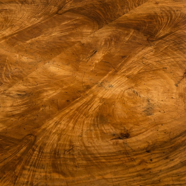 A close-up of the John Richard Cerejeira Desk 77" worn wooden surface showcases visible grain patterns and scratches. With a rich, warm brown color and swirling textures, it serves as a refined centerpiece, adding a rustic yet luxurious touch to any home office.