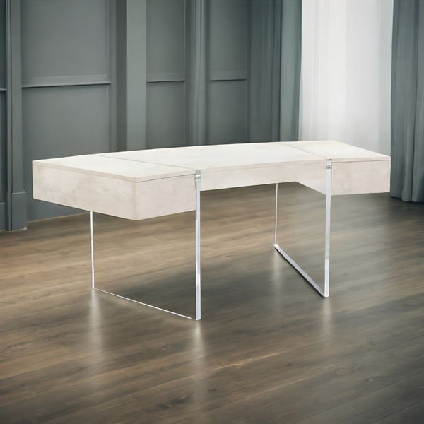 The John Richard Loftus Desk with Side Drawers 77" by John Richard is a modern, minimalist luxury desk featuring a light wood surface and sleek reflective metal legs. Positioned in a well-lit room with wooden flooring and gray paneled walls, natural light floods in from an unseen window. The clean and contemporary design of this desk makes it perfect for an elegant home office setting.