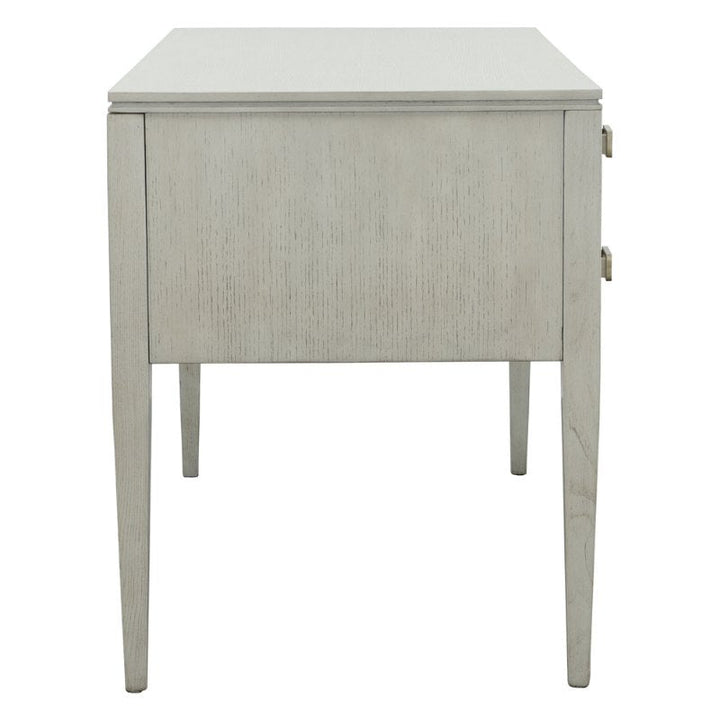 The Fairfield Chair Libby Langdon Patton Desk 54" is a minimalistic piece that exudes modern simplicity, featuring a light gray wooden construction with straight, clean lines and a smooth surface. Accentuated by brass hardware and tapered legs, the design is sleek yet functional. It includes two drawer handles on the right side, finished in an elegant sheer dove gray.