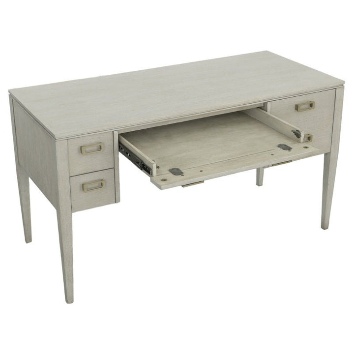 The Libby Langdon Patton Desk 54" by Fairfield Chair boasts a sheer dove gray finish with three drawers on the left side and one drawer on the right. The middle drawer, fitted with brass hardware, is open and pulled out, revealing an additional sliding shelf. The desk features straight, tapered legs for a sleek look.