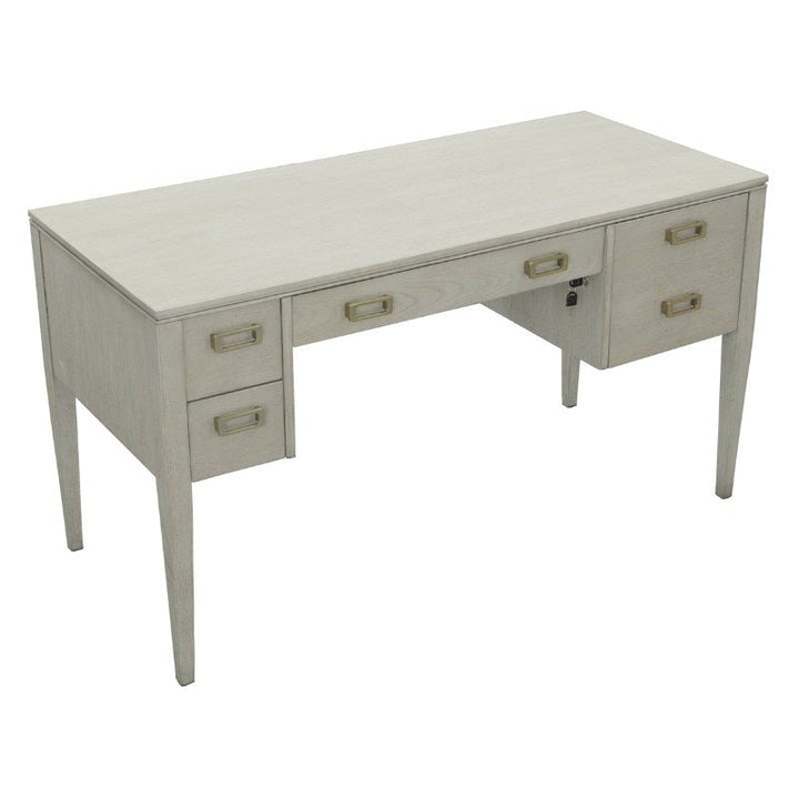 The Libby Langdon Patton Desk 54" by Fairfield Chair is a wooden desk with a sheer dove gray finish. It features five drawers, two on each side and one in the center, each adorned with rectangular brass hardware. The desk boasts a simple, clean design with slim, tapered legs.