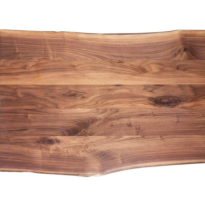 An image of the Live Edge Walnut Waterfall Desk 54" with Trapezoid Base from Fairfield Chair showcases a smooth, polished surface. The American Walnut wood features a rich, warm brown color with natural grain patterns and knots that enhance its organic appearance. Ideal as a home office desk, the edges are irregular, following the natural contour of the wood.