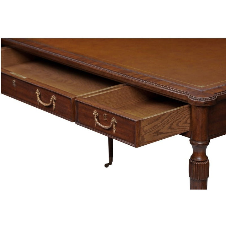 The Mahogany Leather Top Writing Desk by Aston Court is an antique piece featuring ornate detailing, a spacious mahogany leather top, and two open drawers adorned with brass handles. Its timeless design includes one visible tapered, fluted leg with intricate carvings, and the wood boasts a rich, polished finish.