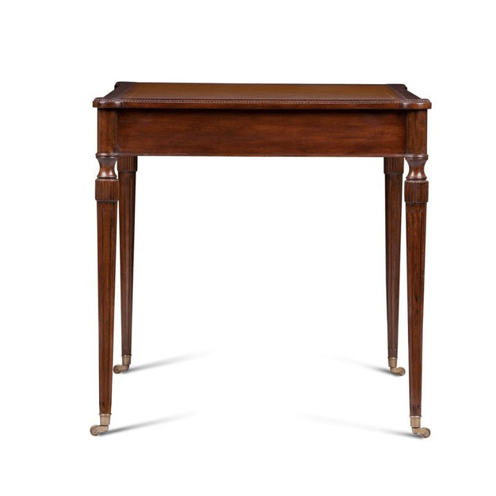 The Mahogany Leather Top Writing Desk by Aston Court is an elegant rectangular wooden table with carved details and a timeless design. It features tapered legs with brass caps on the feet. Reminiscent of classic writing desks, its simple and classic aesthetic makes it suitable for a variety of interior settings.