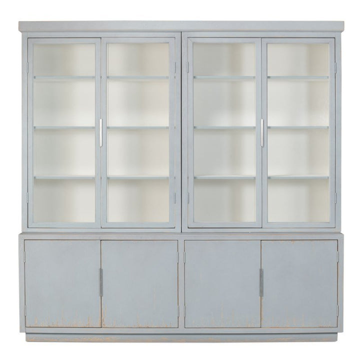 A large, Eros Blue wooden cabinet with a distressed finish featuring two sections. The upper section has two sets of glass doors revealing shelves inside. The lower section, inspired by the Maldives 4 Door Bookcase design from Sarreid, has four solid doors without glass, providing additional storage.