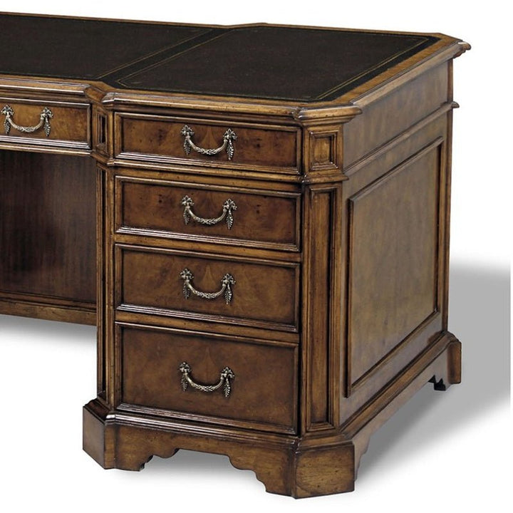 The Myrtle Writing Desk from Aston Court, a vintage piece, features ornate brass handles on four drawers. It has an antique leather top and carved details on the edges, lending it a classic and elegant appearance. The desk rests on short, sturdy legs with beveled base trim.