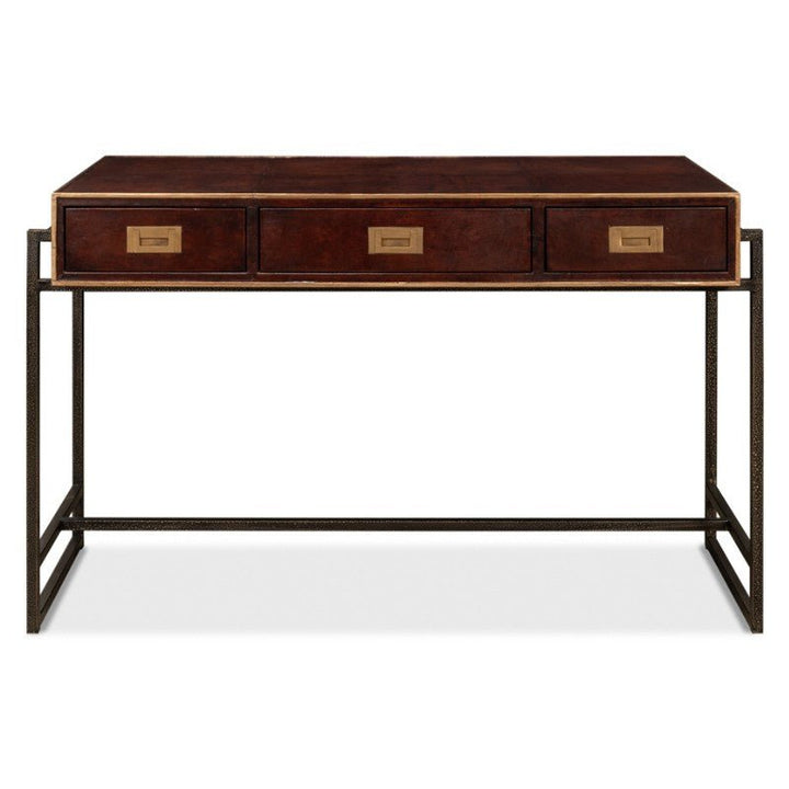 The Old Leather Desk by Sarreid features a hand-colored leather top and three central drawers adorned with brass handles. The desk boasts a dark stain finish on the wood and sits on an iron frame with a rectangular base, giving it a modern industrial look with transitional style flair.