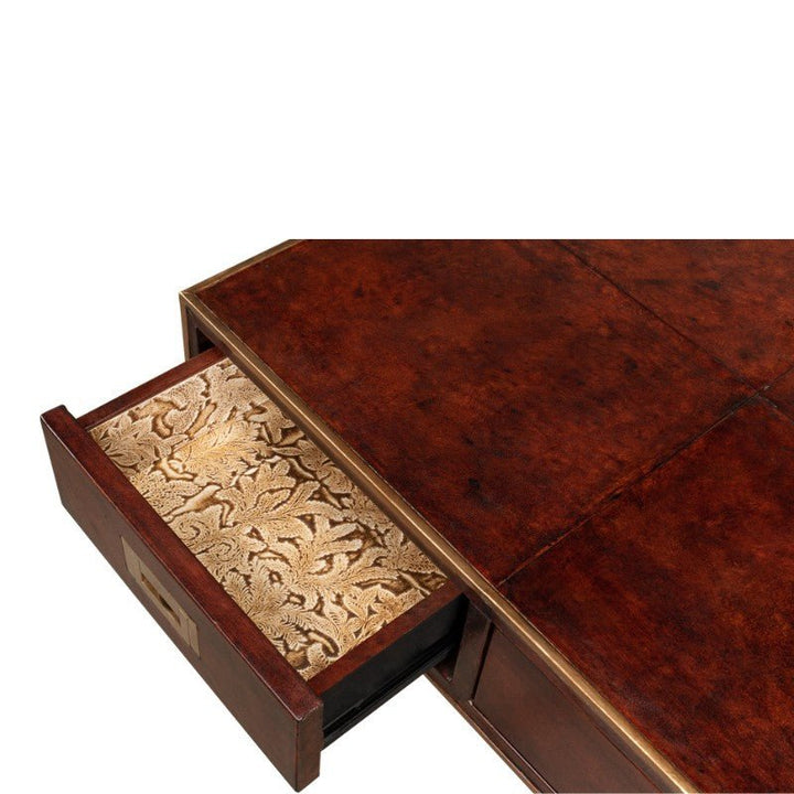 A richly colored wooden table with a corner drawer partially open, its interior lined with light-colored fabric featuring a gold floral pattern. The table's dark, polished finish evokes the charm of the Old Leather Desk with an iron frame from Sarreid, blending traditional elegance with transitional style.